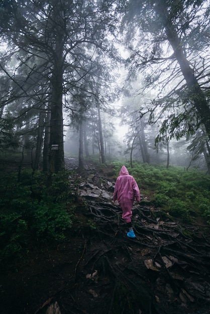 Gratis foto jonge vrouw in een regenjas loopt door het bos in de regen