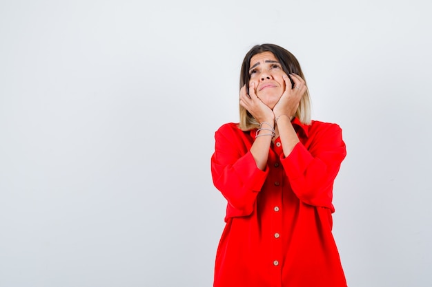 Jonge vrouw in een rood oversized shirt dat de kin op de handen steunt en er attent uitziet, vooraanzicht.