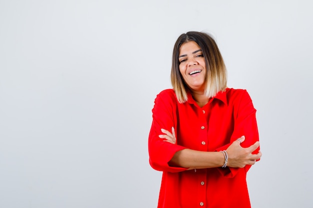 Jonge vrouw in een rood oversized shirt dat met gekruiste armen staat en er zelfverzekerd uitziet, vooraanzicht.