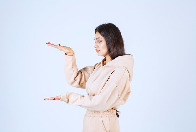 Jonge vrouw in een roze hoodie die de hoeveelheid of de grootte van een voorwerp toont