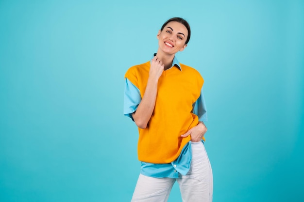 Jonge vrouw in een shirt en een oranje vest op een turquoise achtergrond lacht vrolijk, kijkt naar de camera