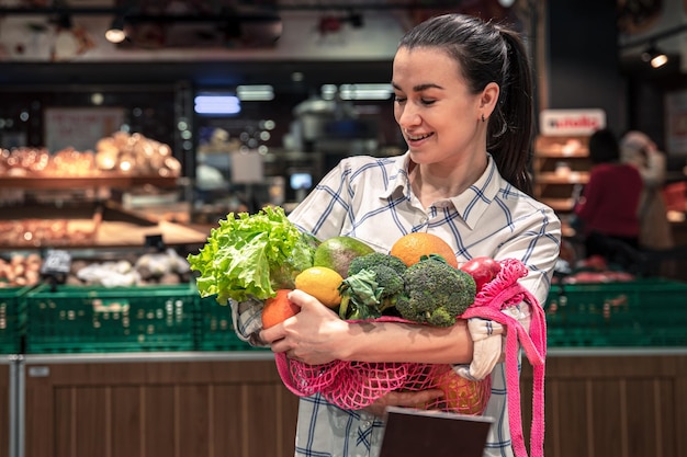 Jonge vrouw in een supermarkt met groenten en fruit die boodschappen koopt