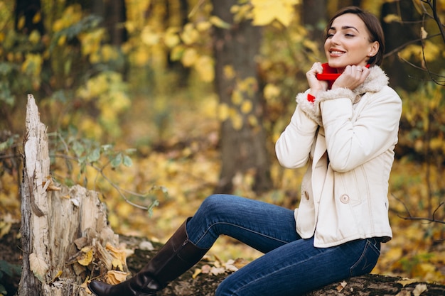 Gratis foto jonge vrouw in een zitting van het de herfstpark op een logboek