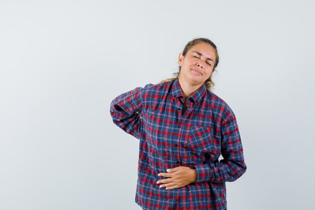 Jonge vrouw in gecontroleerd overhemd dat buikpijn heeft en uitgeput kijkt