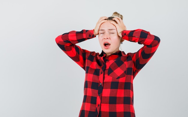 Jonge vrouw in gecontroleerd overhemd hand in hand op het hoofd en op zoek geïrriteerd