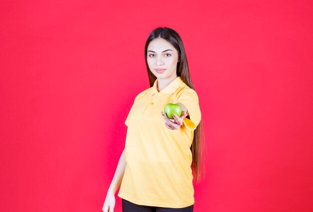 Jonge vrouw in geel shirt die een groene appel vasthoudt en er een aanbiedt aan de klant