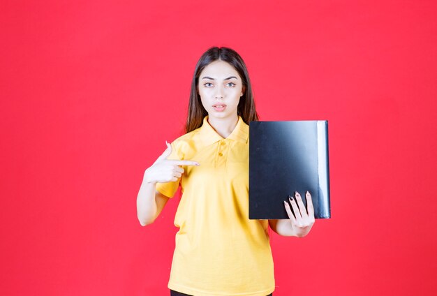 Jonge vrouw in geel shirt met een zwarte map en positief handteken