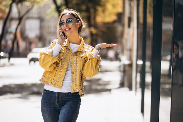 Jonge vrouw in gele jas met behulp van telefoon buiten in de straat