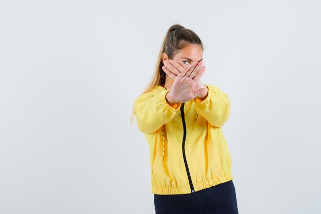 Jonge vrouw in gele regenjas die stopgebaar met gekruiste handen toont en ernstig kijkt