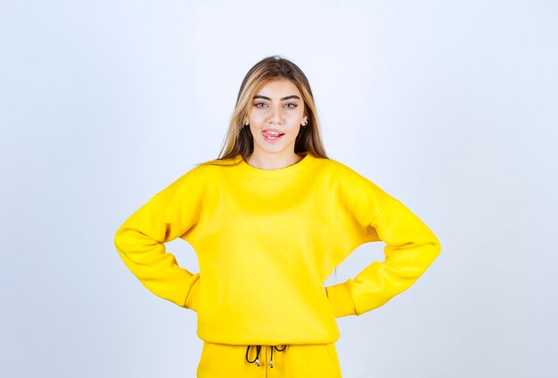 Jonge vrouw in gele trainingspak poseren voor camera over witte muur