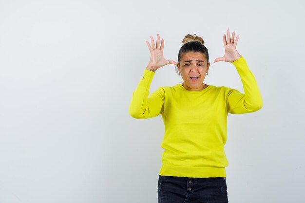 Jonge vrouw in gele trui en zwarte broek die haar handen uitstrekt in overgavepositie en er gehaast uitziet