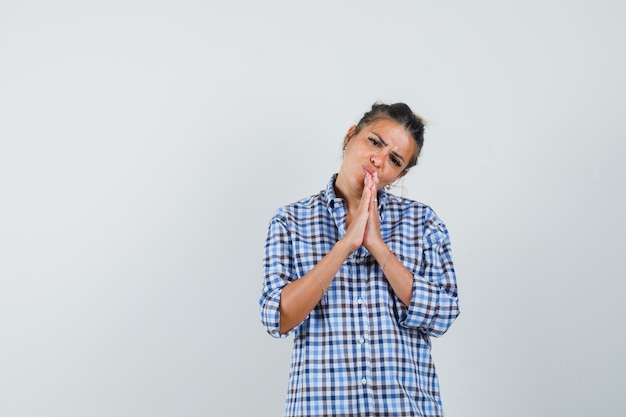 Jonge vrouw in geruit overhemd biddend gebaar tonen en hoopvol kijken.