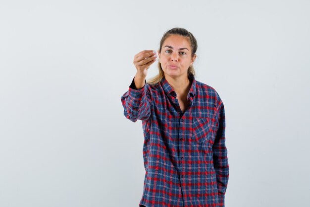 Jonge vrouw in geruit overhemd die hand uitrekt als iets vasthoudt en ernaar kijkt en gefocust kijkt