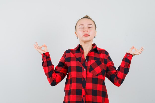 Jonge vrouw in geruit overhemd die meditatie met gesloten ogen doen en ontspannen kijken