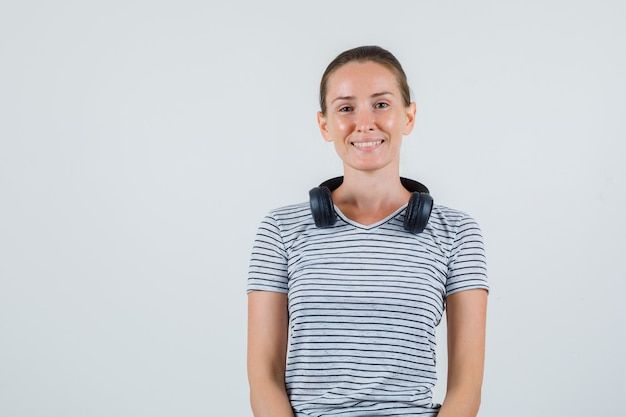 Jonge vrouw in gestreept t-shirt, koptelefoon en op zoek vrolijk, vooraanzicht.