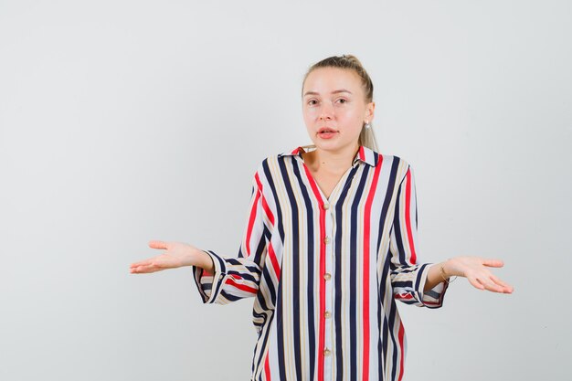 Jonge vrouw in gestreepte blouse die haar schouders ophaalt en verward kijkt