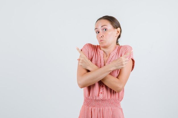 Jonge vrouw in gestreepte jurk wijst naar kant en kijkt verbaasd, vooraanzicht.