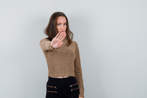 Jonge vrouw in goud vergulde sweater en zwarte broek die stopgebaar toont en ernstig kijkt