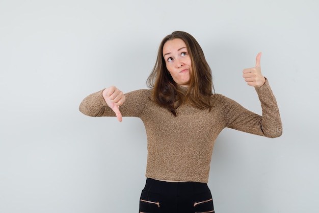 Jonge vrouw in gouden blouse die duim op en neer toont en verbaasd kijkt