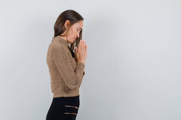 Jonge vrouw in gouden blouse die en hoopvol bidden kijkt. vrije ruimte voor uw tekst