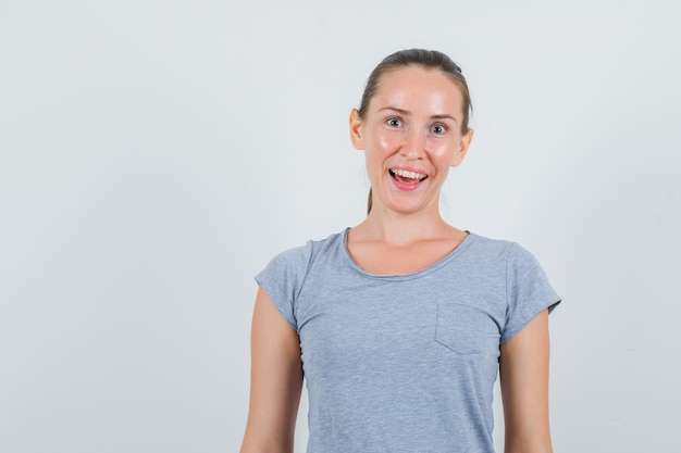 Jonge vrouw in grijs t-shirt en op zoek vrolijk, vooraanzicht.