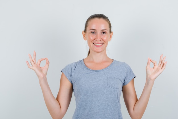 Gratis foto jonge vrouw in grijs t-shirt meditatie doen en glimlachen, vooraanzicht.