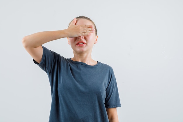 Jonge vrouw in grijze t-shirt die ogen behandelt met hand en opgewekt kijkt