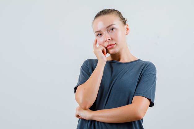 Jonge vrouw in grijze t-shirt leunende wang aan kant en peinzend kijkt