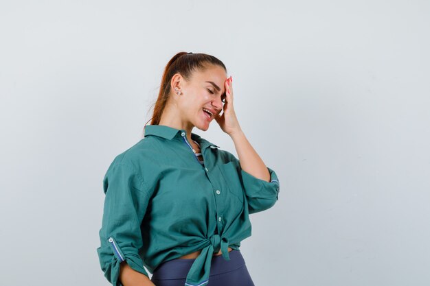 Jonge vrouw in groen overhemd met hand op gezicht en vergeetachtig, vooraanzicht.