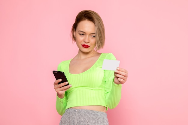 jonge vrouw in groen shirt en grijze broek met telefoon en witte kaart