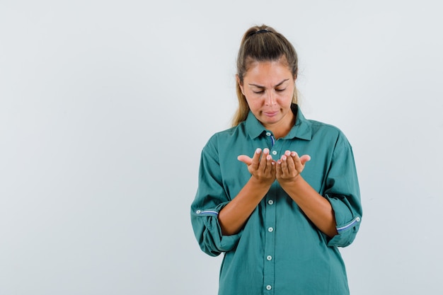 Gratis foto jonge vrouw in groene blouse die handen uitrekt als iets denkbeeldigs vasthoudt en ernaar kijkt en gefocust kijkt