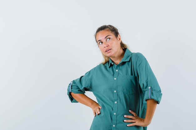 Jonge vrouw in groene blouse hand in hand op taille en peinzend op zoek