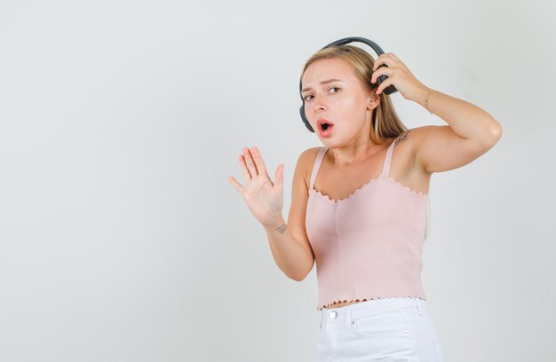 Jonge vrouw in hemd, minirok die hoofdtelefoons met stopgebaar opstijgt en bezorgd kijkt