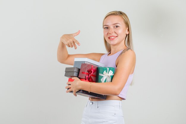 Jonge vrouw in hemd, minirok wijzende vinger naar geschenkdozen en ziet er vrolijk uit