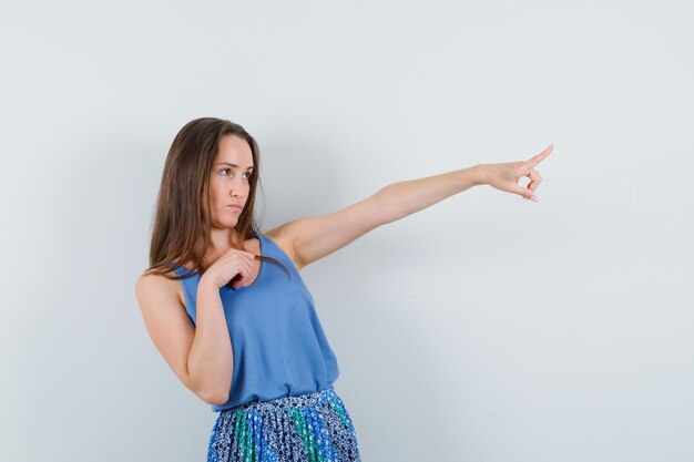 Jonge vrouw in hemd, rok wijst weg en kijkt gefocust, vooraanzicht.