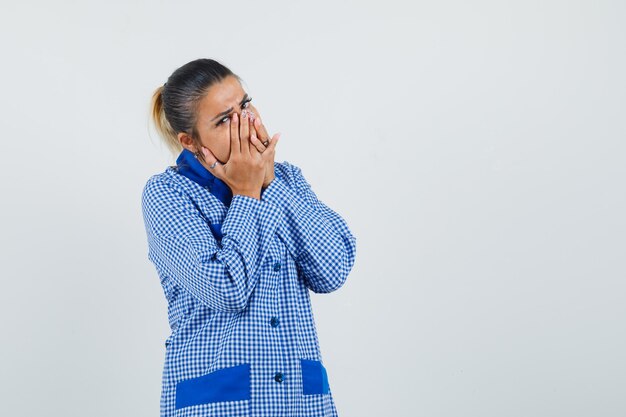 Jonge vrouw in het blauwe overhemd die van de gingangpyjama mond met handen behandelen en verbaasd, vooraanzicht kijken.