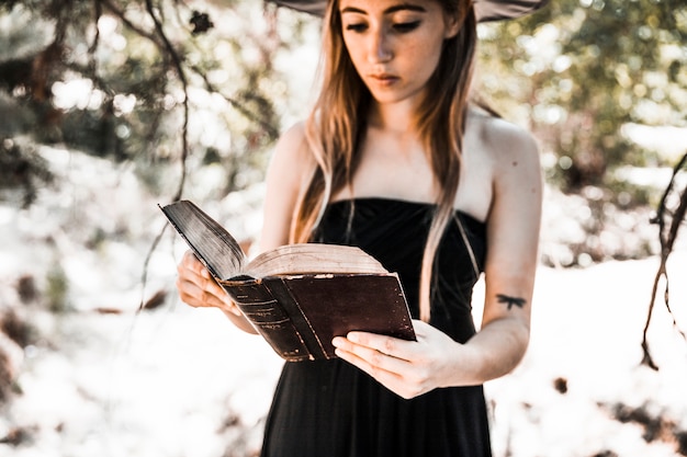 Gratis foto jonge vrouw in het boek van de hoedenlezing in bos