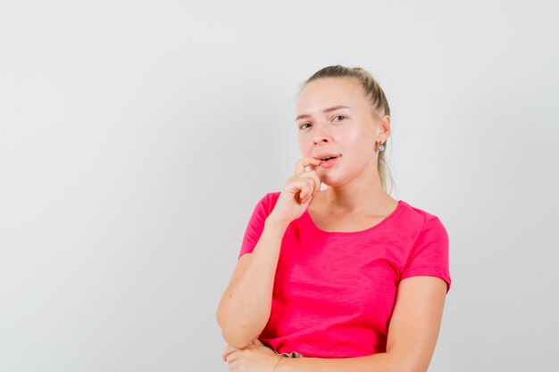 Jonge vrouw in het denken poseren in roze t-shirt en op zoek verstandig