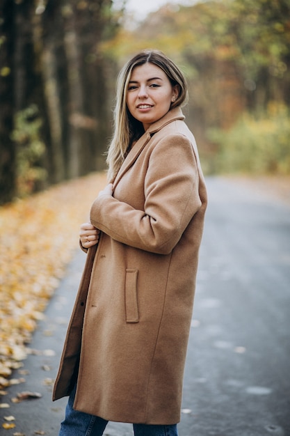 Jonge vrouw in jas die zich op de weg in een de herfstpark bevindt
