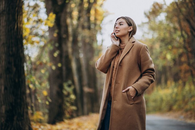 Jonge vrouw in jas die zich op de weg in een de herfstpark bevindt