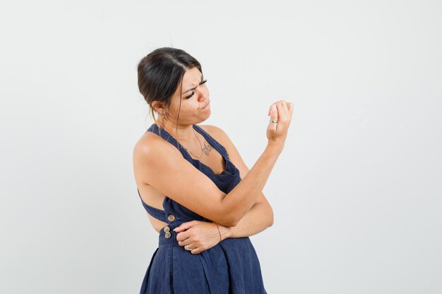 Jonge vrouw in jurk die naar haar nagels kijkt en peinzend kijkt