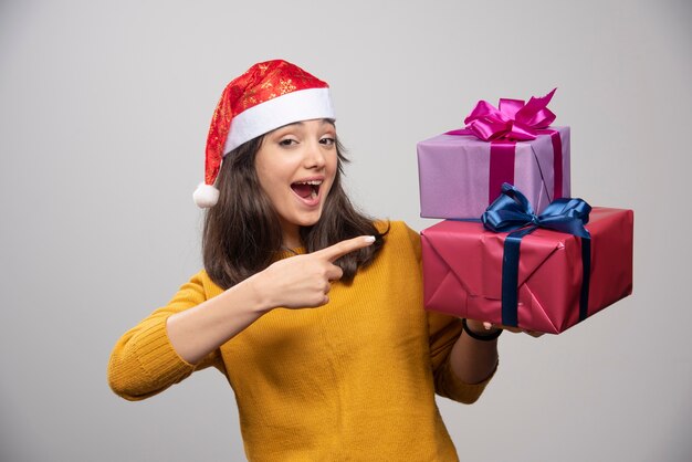 Jonge vrouw in kerstmuts tonen op kerstcadeautjes.