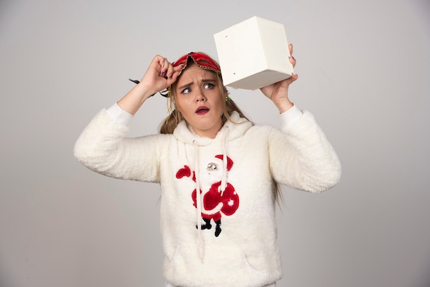 Jonge vrouw in kerstsweatshirt die geschenkdoos bekijkt.