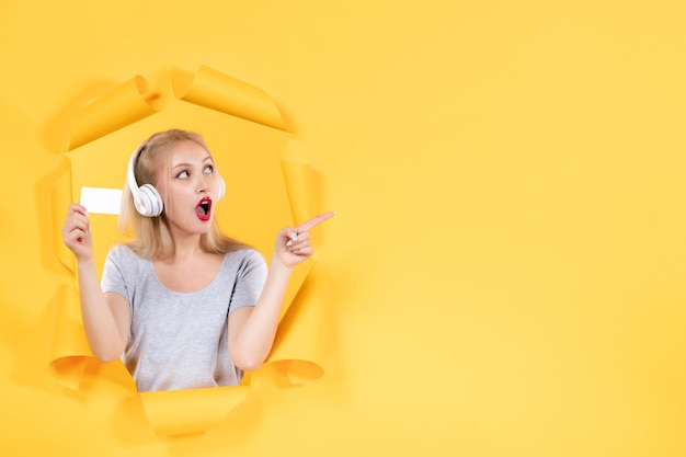 Jonge vrouw in koptelefoon met creditcard op gele muur