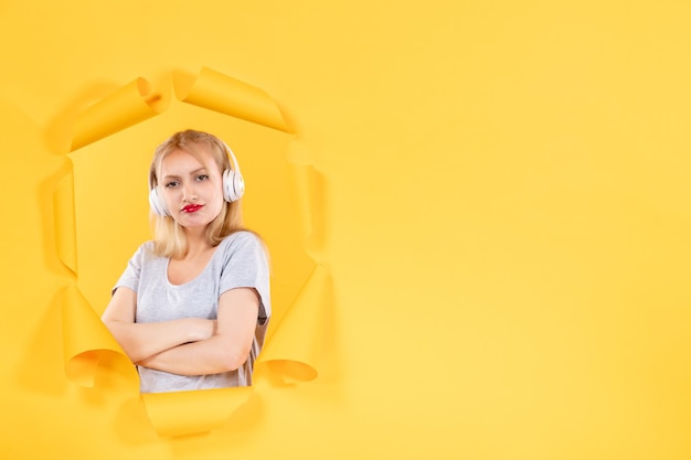 Jonge vrouw in koptelefoon met gekke uitdrukking op gele muur