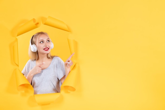 Jonge vrouw in koptelefoon op de gescheurde gele papieren achtergrond audio echografie muziek geluid