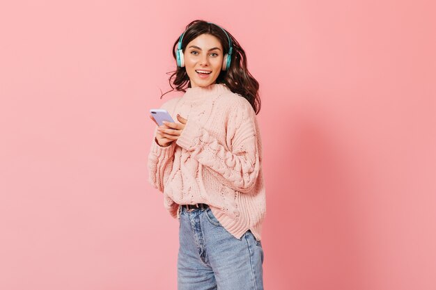 Jonge vrouw in lichtgekleurde moeder jeans is dansen en luisteren naar vrolijk lied in blauwe koptelefoon.