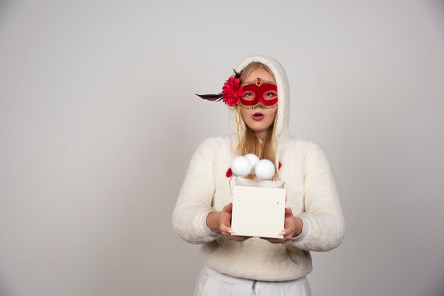 Gratis foto jonge vrouw in maskerademasker met geschenkdoos met een stel ballen.