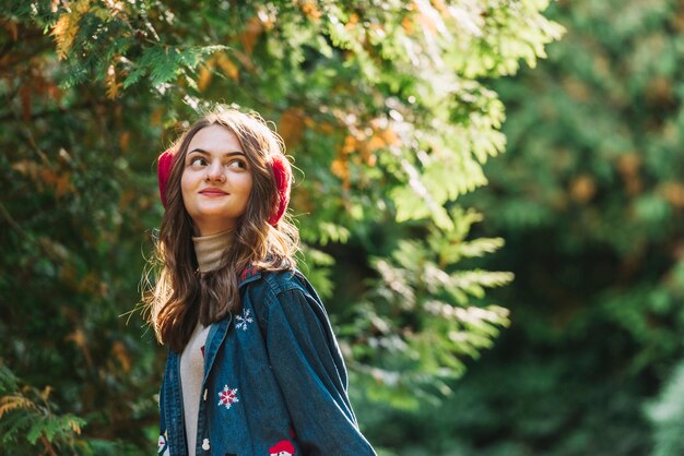 Jonge vrouw in oorbeschermers dichtbij groene takjes