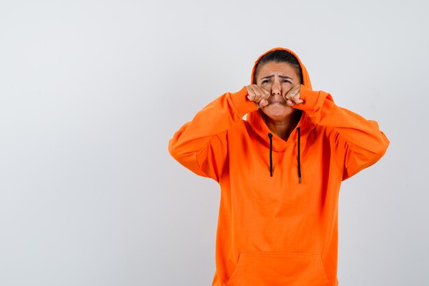 Jonge vrouw in oranje hoodie die vuisten balt en er verdrietig uitziet?